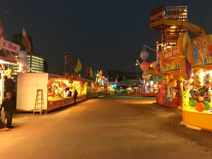 A lit-up funfair at night with an empty midway and no queues at the stalls or rides